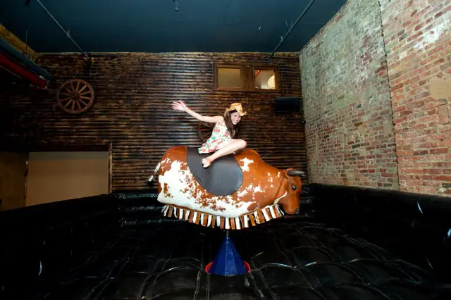 Photographer Katie Sokoler rides a bull and photographs herself all at the same time.